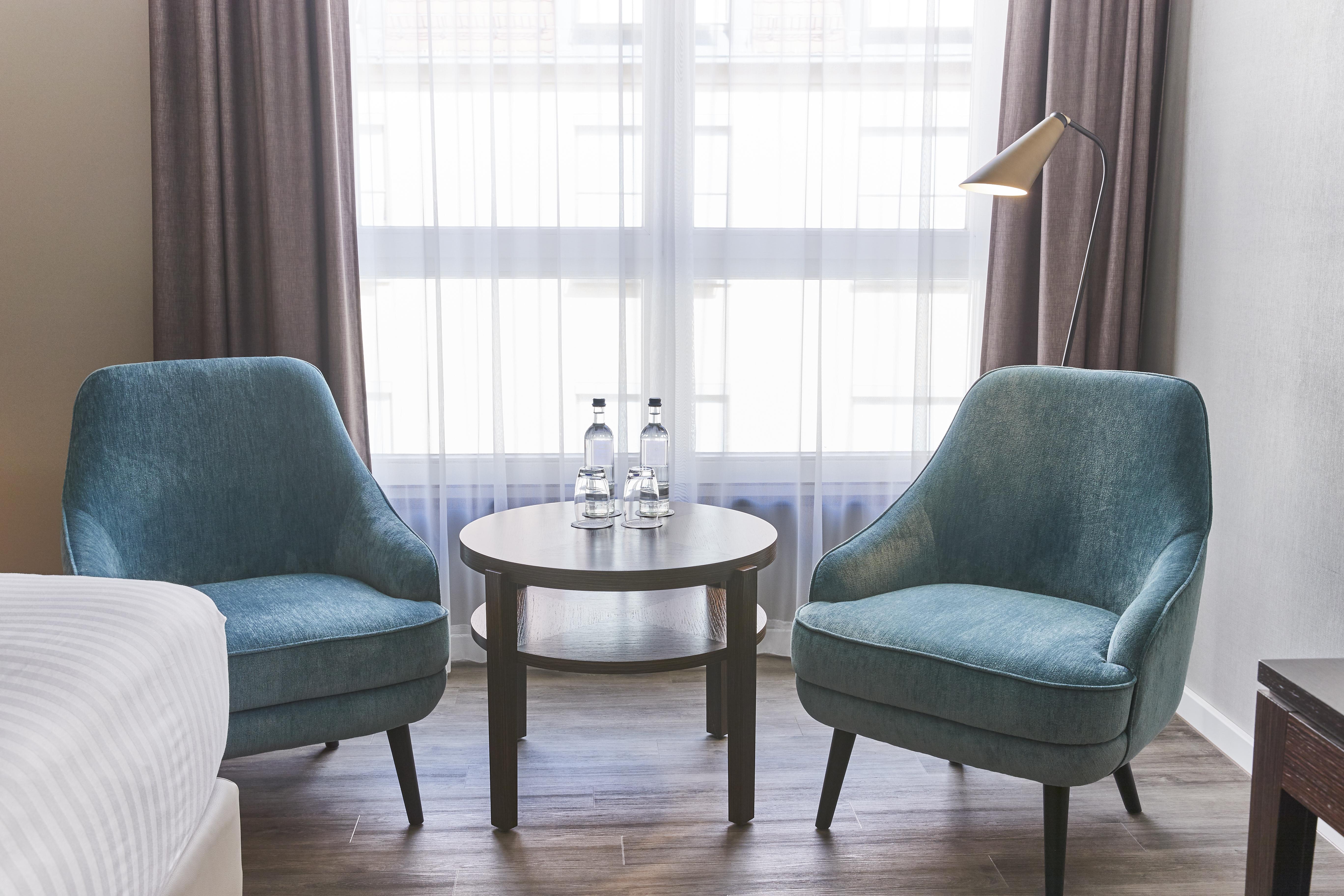 Steigenberger Hotel De Saxe Dresden Exterior photo The photo shows a cozy seating area featuring two light blue upholstered chairs, each with a curved back and tapered wooden legs. In the center, there is a small round table with a dark wood finish. On the table, there are two glass bottles of water.